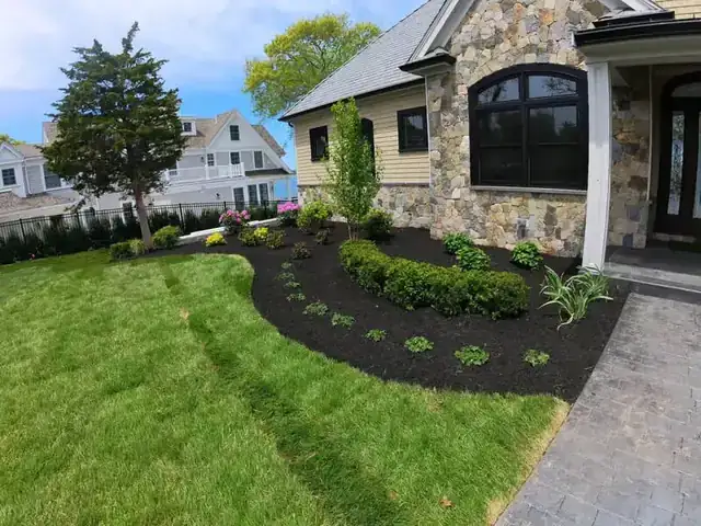 Freshly landscaped lawn with mulched beds in front of a stone and shingle home