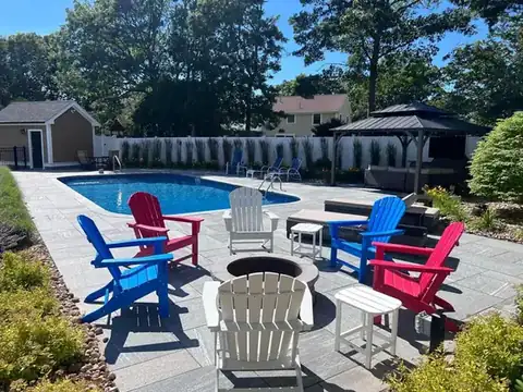 Pool surrounded by gray paver patio with colorful chairs