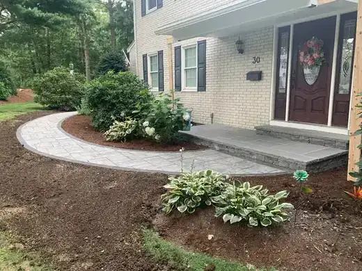 A paver walkway curving past hostas and fresh mulch to a front door